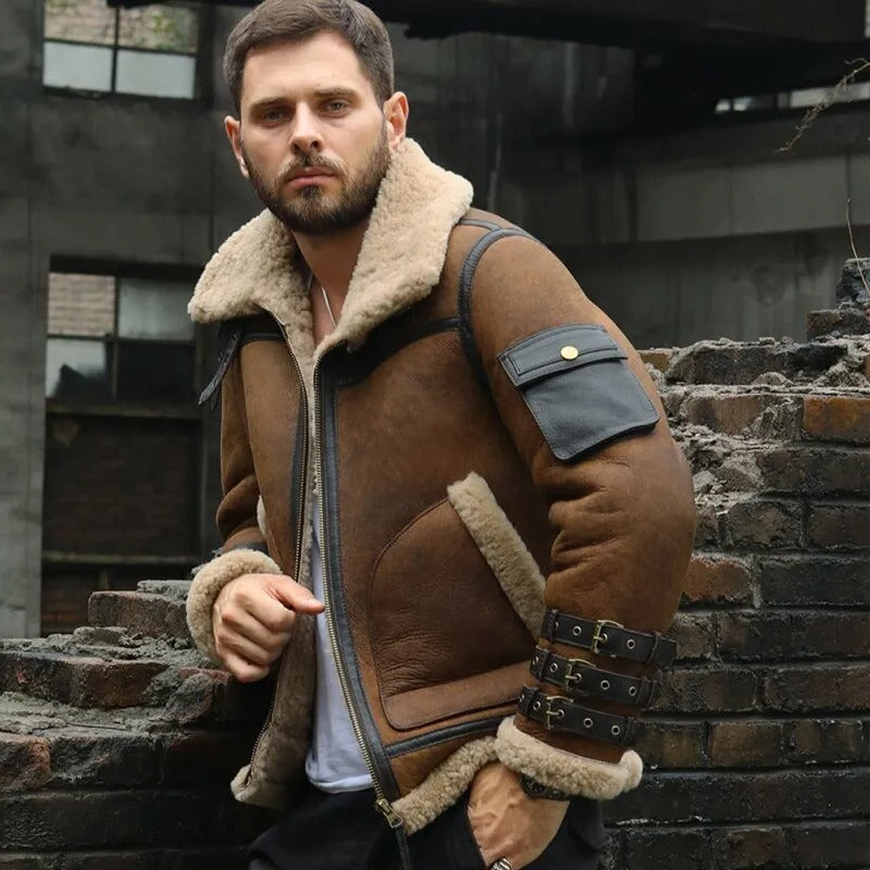 Man wearing a brown shearling jacket standing in front of a brick wall.