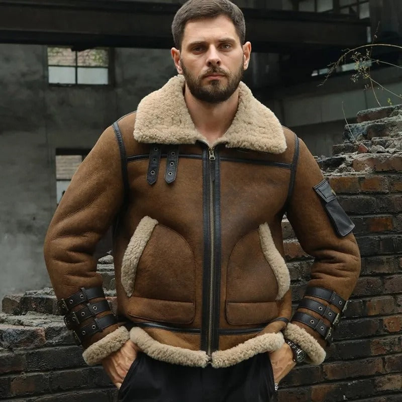 Man wearing a brown shearling jacket standing in front of a brick wall.