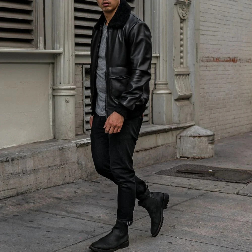 Person wearing a black leather jacket and pants walking on a sidewalk.