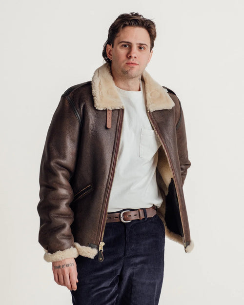 Man wearing a brown leather jacket with fur trim on a white background