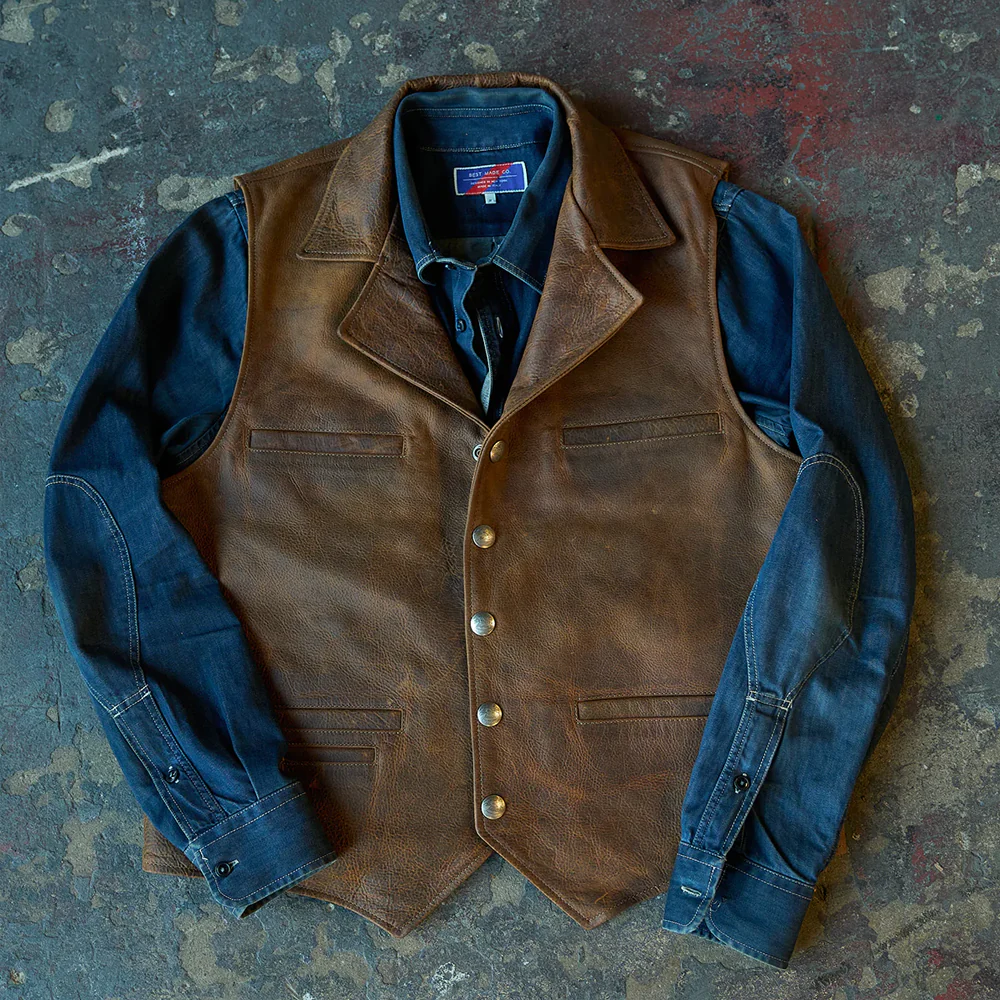 Brown leather vest with blue shirt and denim jacket on a textured surface