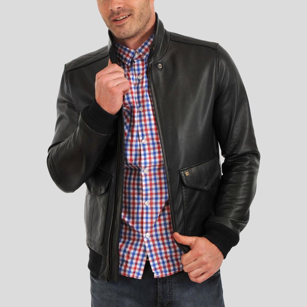 Man wearing a black leather jacket over a red, blue, and white checkered shirt on a gray background