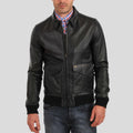 Man wearing a black leather jacket over a checkered shirt on a gray background