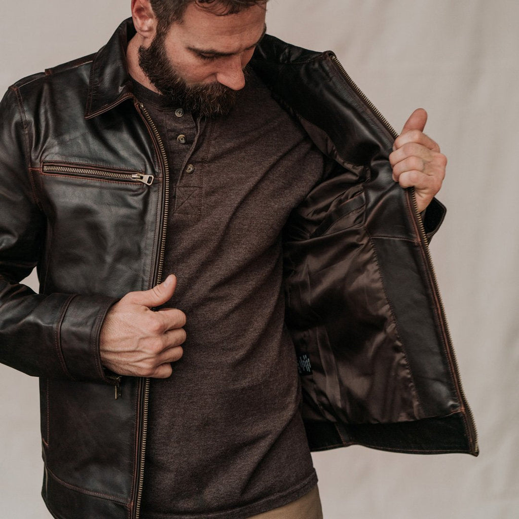 Man wearing a brown leather jacket over a dark shirt against a neutral background