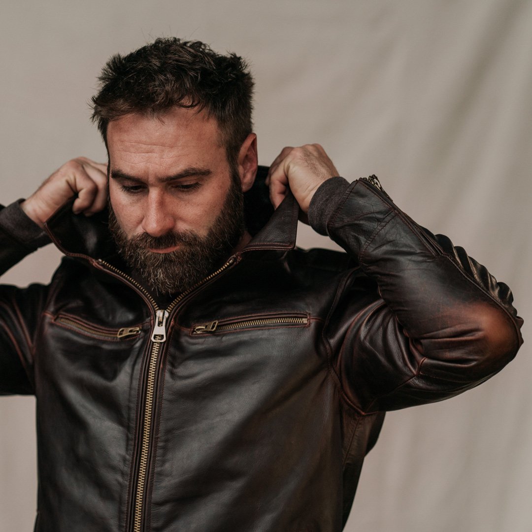 Man adjusting his leather jacket against a neutral background