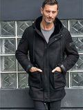 Man wearing a black coat standing in front of a glass block wall.