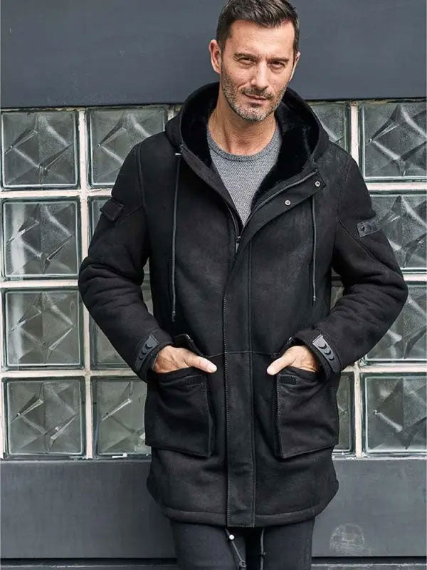 Man wearing a black coat standing in front of a glass block wall.