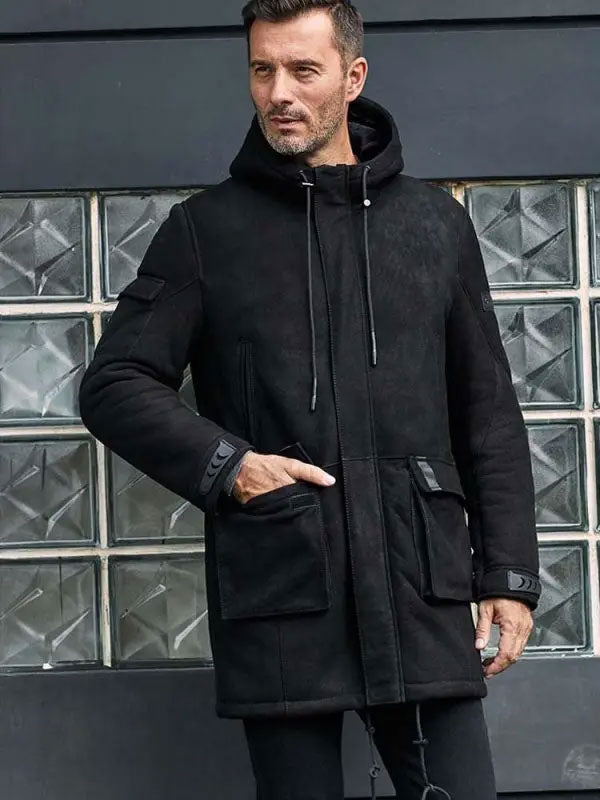 Man wearing a black coat standing in front of a glass block wall.