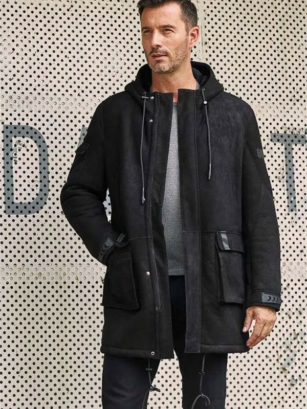 Man wearing a black coat against a patterned wall