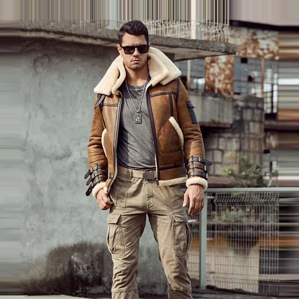 A man wearing a brown shearling-lined aviator jacket with beige cargo pants, sunglasses, and a silver necklace, standing in an urban outdoor setting.