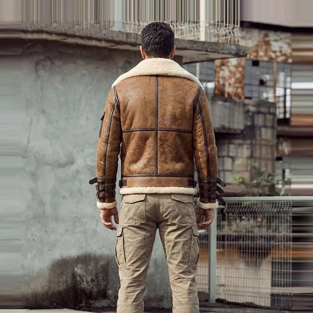 A man viewed from behind wearing a brown shearling-lined aviator jacket with dark trim and tan cargo pants, standing in an urban outdoor setting.
