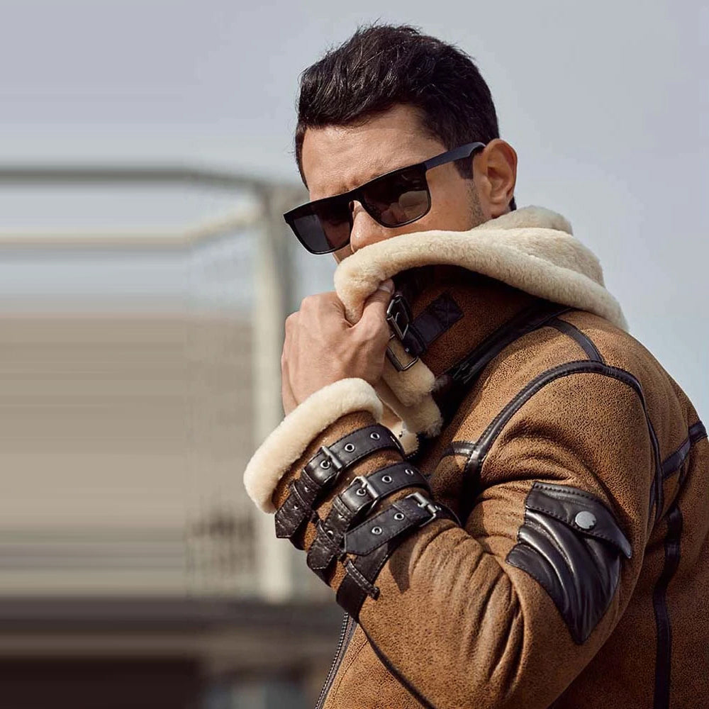 Man wearing a brown coat with fur-lined hood and leather gloves, holding his face.