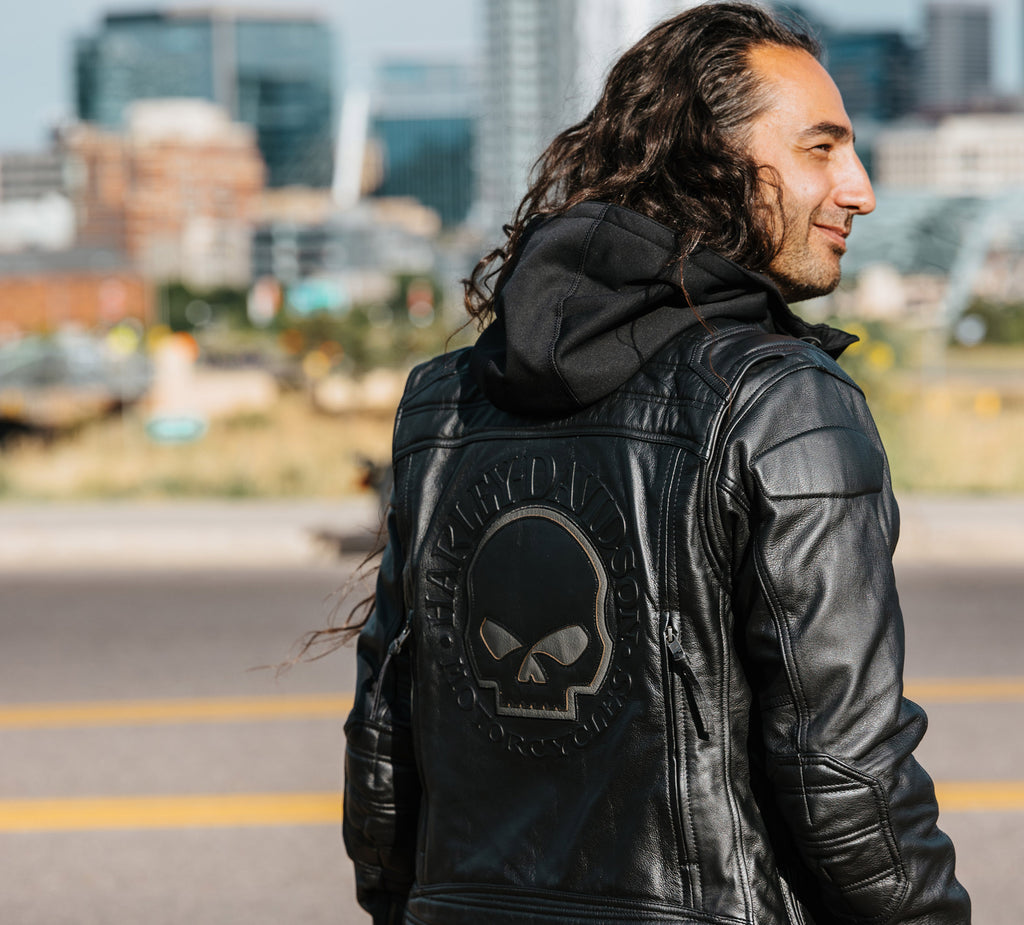 Man wearing a black leather jacket with a skull emblem in an urban setting