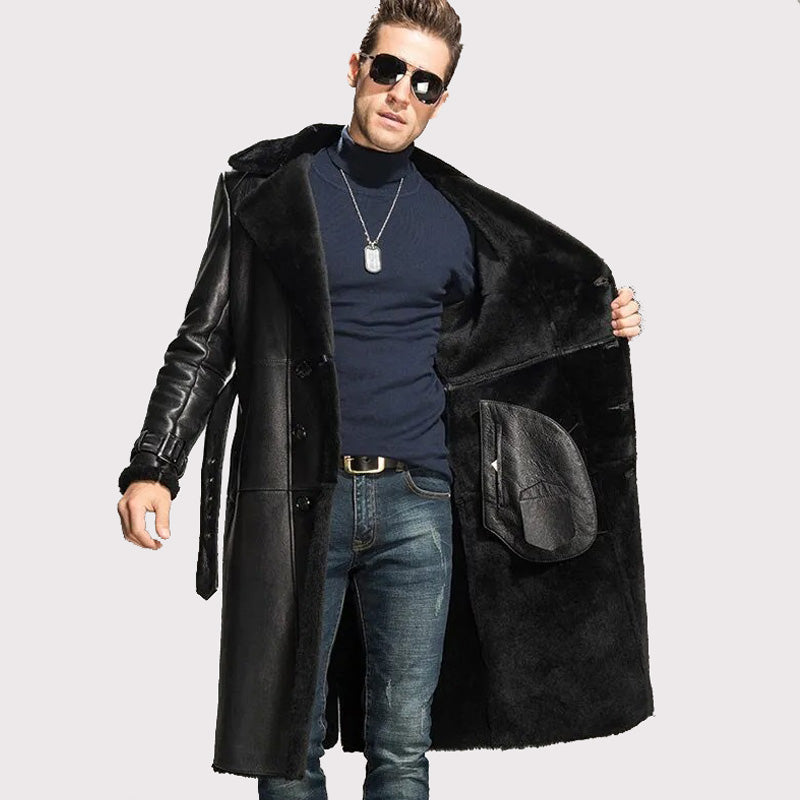 Man wearing a long black coat, sunglasses, and a blue shirt on a light gray background