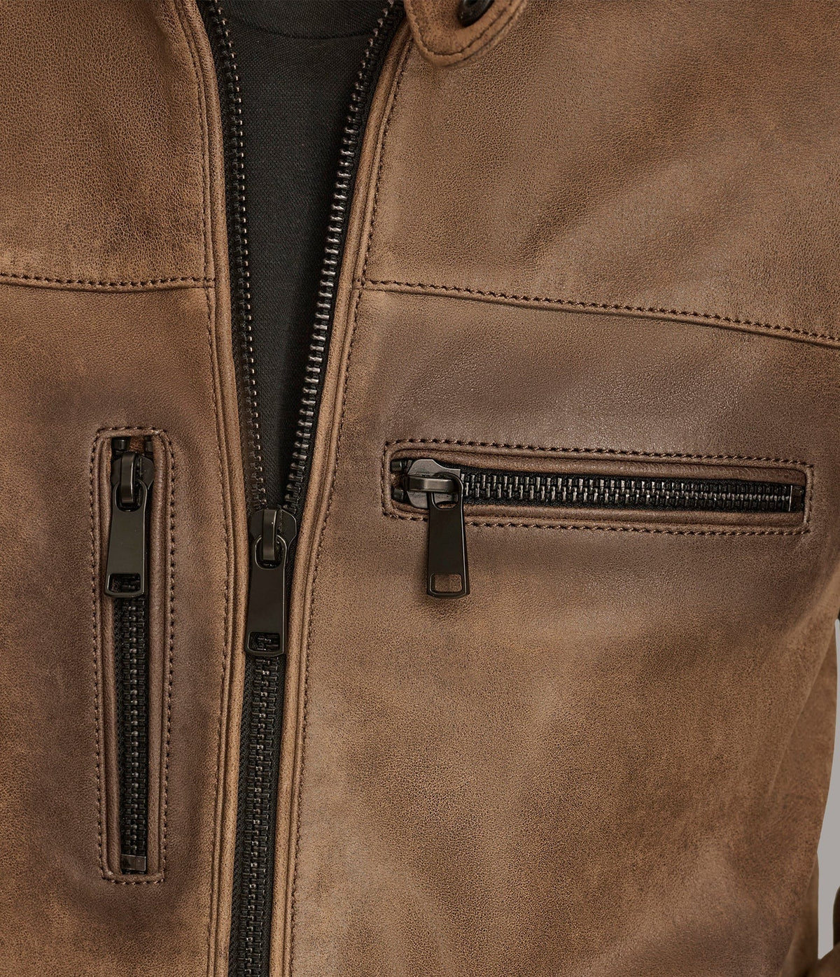 Close-up of a brown leather jacket showing the front zipper, a zippered chest pocket, and a vertical zip pocket with black zippers and dark metal pulls.
