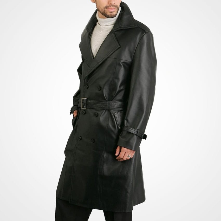 A man wearing a black leather double-breasted trench coat with a matching belt, styled over a light gray turtleneck sweater, photographed against a plain white studio background.