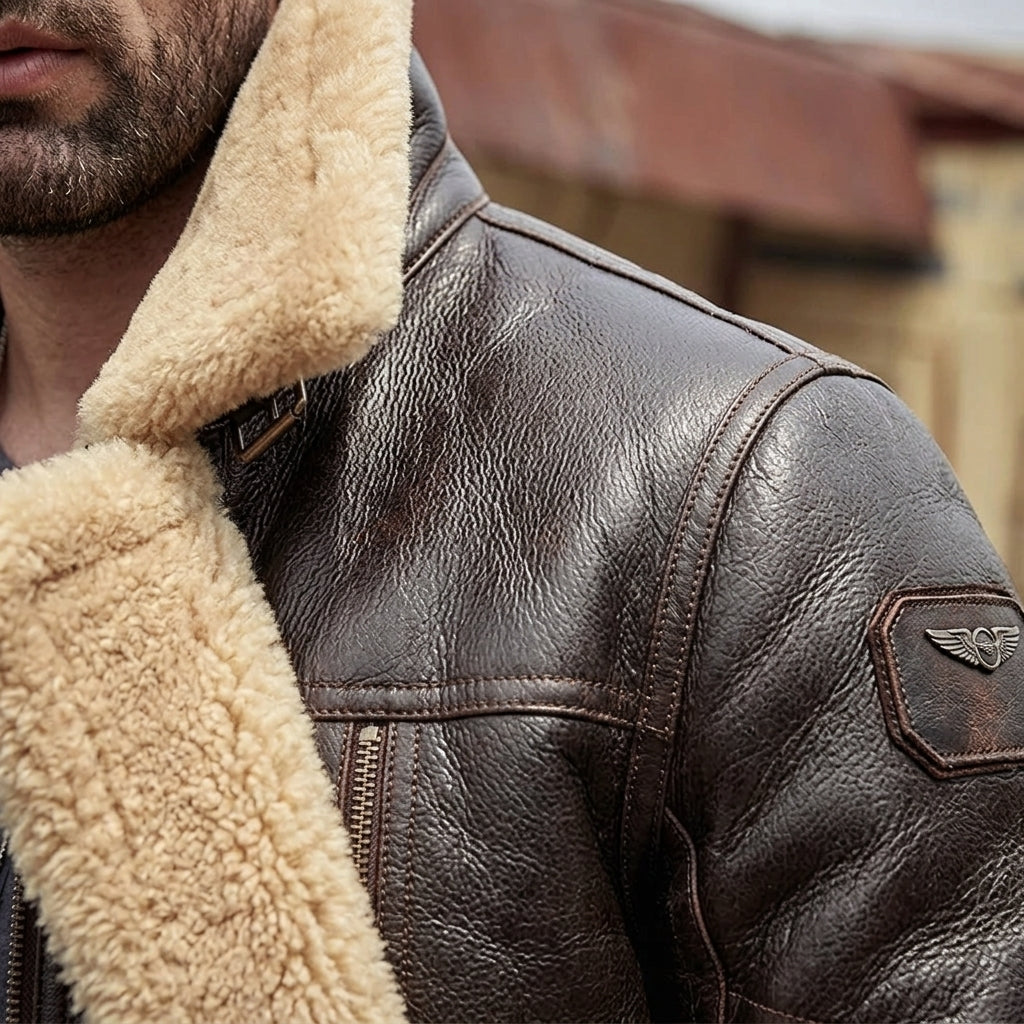 Close-up of a man wearing a brown leather aviator-style jacket with a thick beige shearling collar and a winged emblem patch on the sleeve.