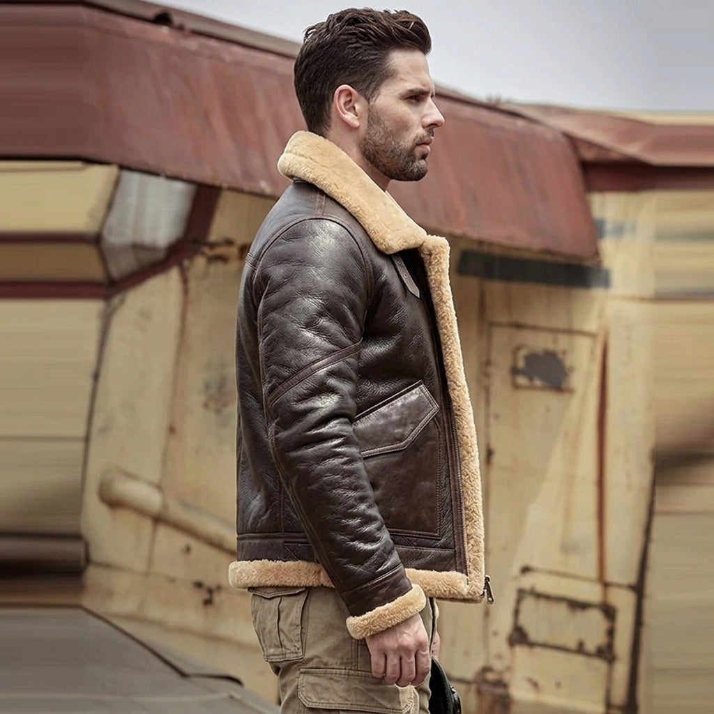 A man wearing a dark brown leather aviator jacket with a beige shearling lining, standing in front of a rustic, weathered building.