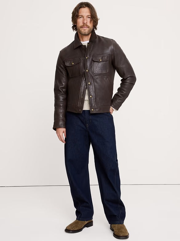 Man wearing a brown leather jacket and dark jeans on a white background