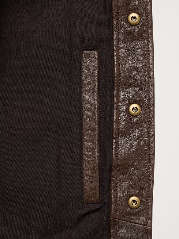 Close-up of a dark brown jacket or overshirt showing a dark brown fabric body, a textured brown leather-like vertical panel, and three brass snap buttons on the right side.