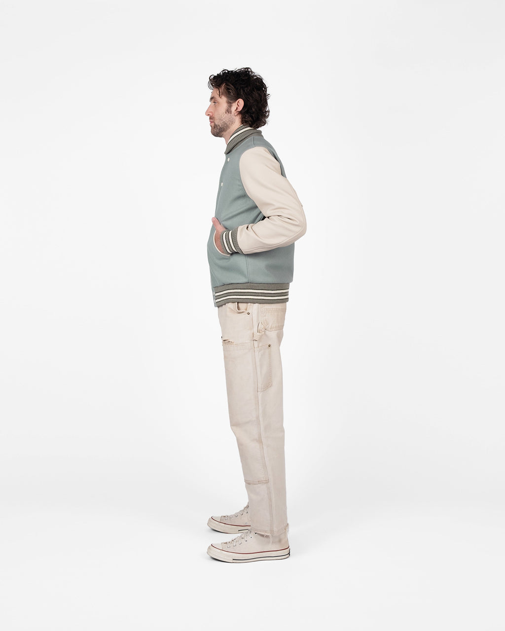Man wearing a gray vest over a beige sweater with beige pants on a white background