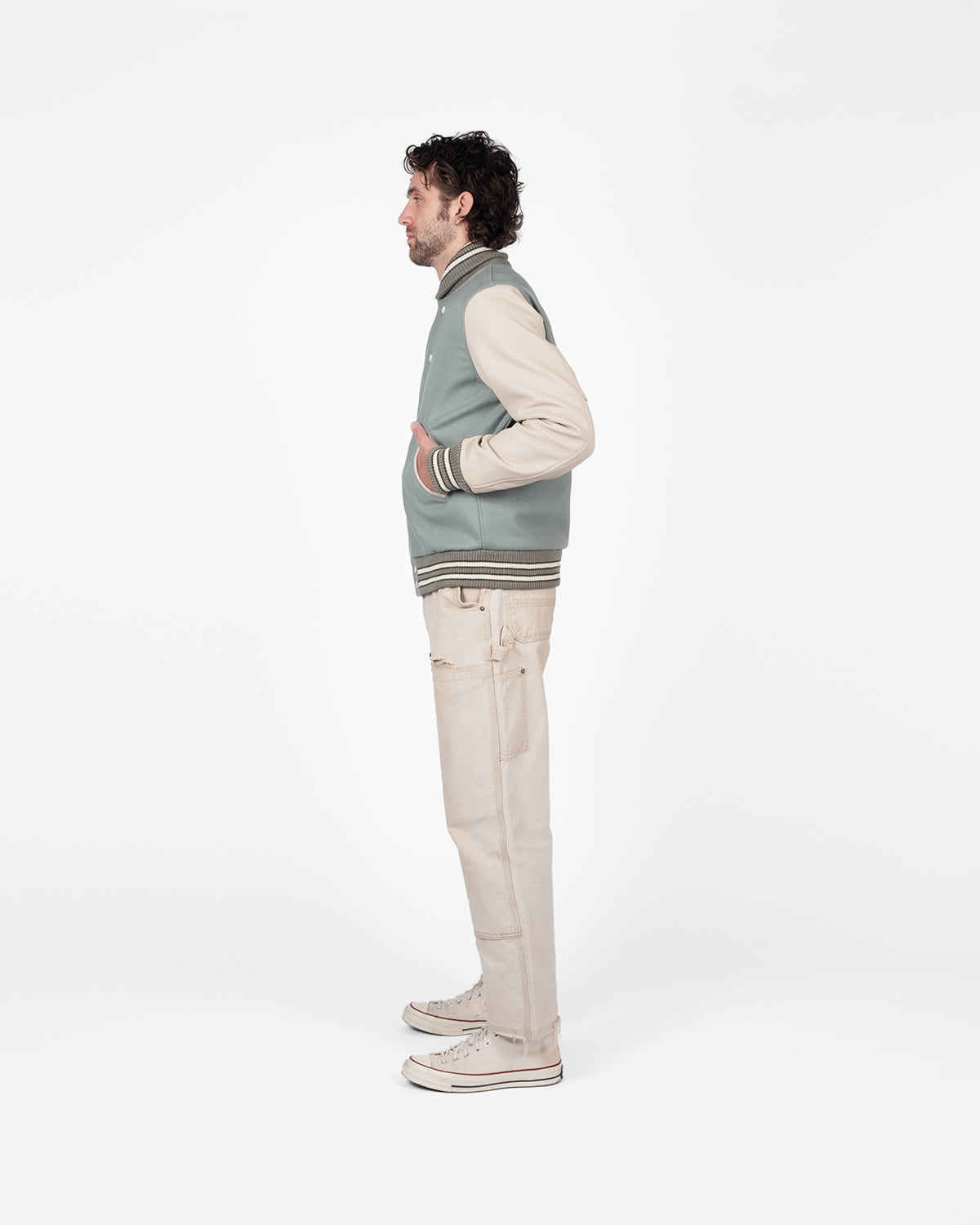 Man wearing a gray vest over a beige sweater with beige pants on a white background