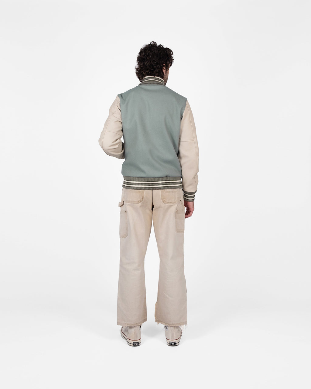Person wearing a light gray vest over a beige shirt with beige pants on a white background
