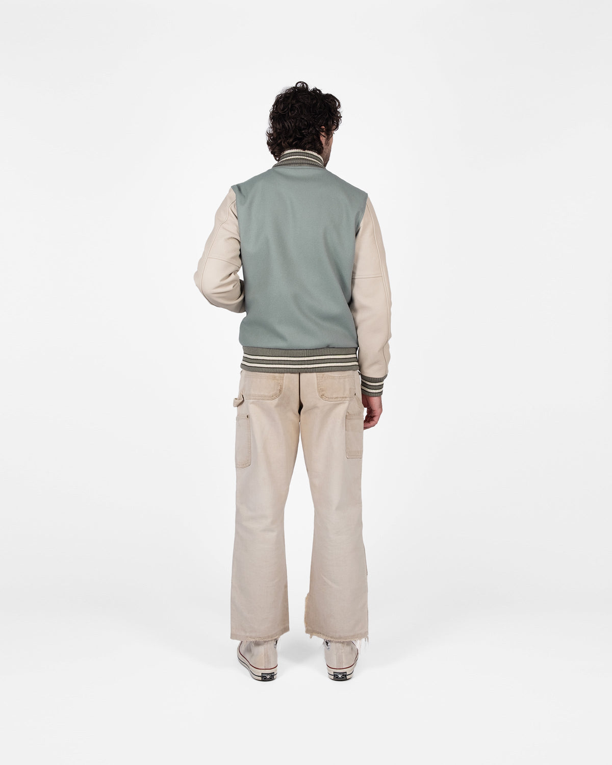 Person wearing a light gray vest over a beige shirt with beige pants on a white background