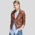 Woman wearing a brown leather jacket over a light blue shirt on a plain background