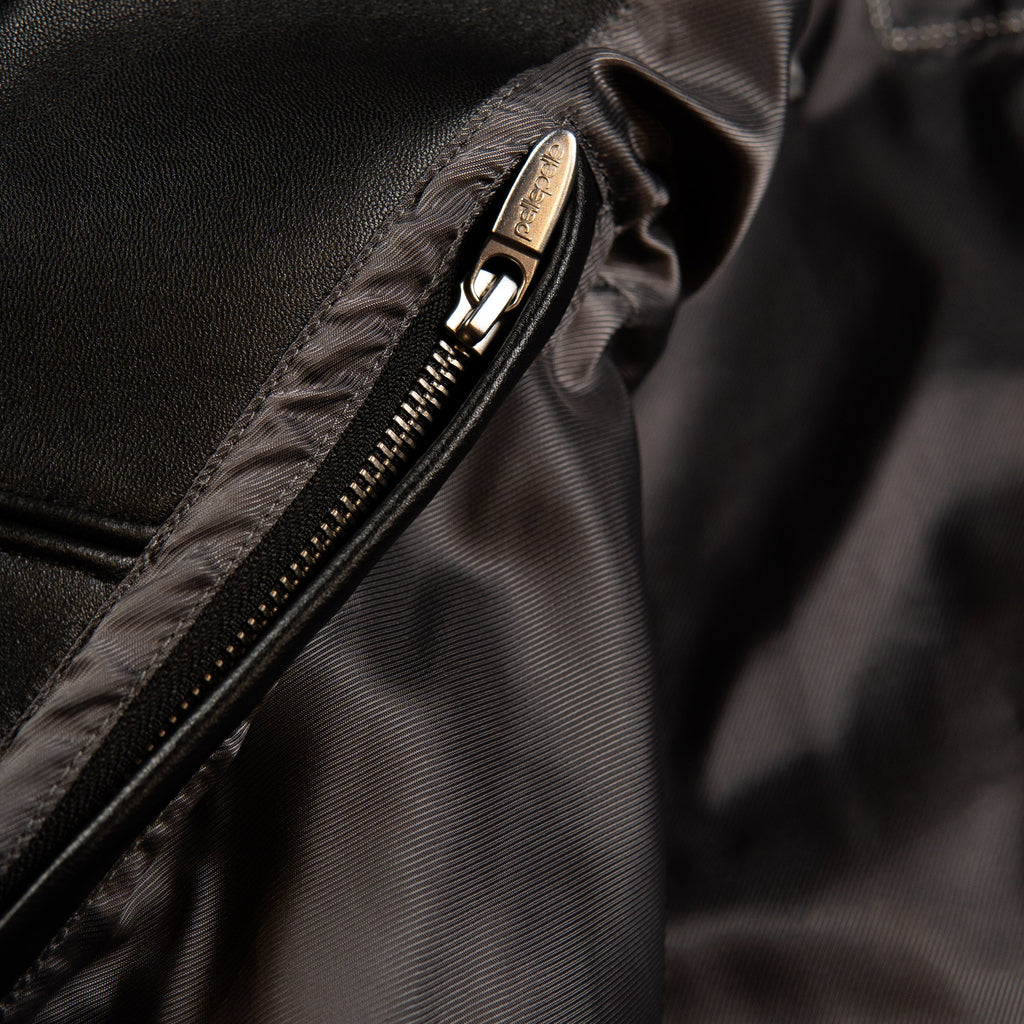 Close-up of a black nylon garment with a silver metal zipper, showing the zipper pull engraved with 'PELLE'.