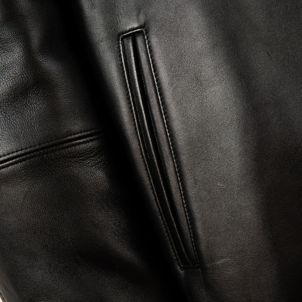 Close-up of a black leather jacket showing a vertical zippered pocket and stitched panel details.