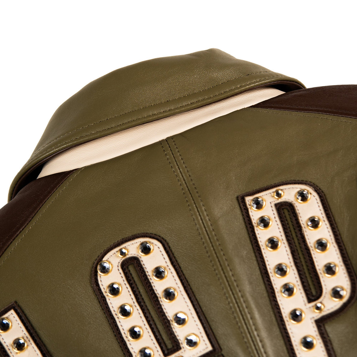 Close-up of the back of an olive green leather jacket with dark brown shoulder panels and large cream-colored studded letter patches.