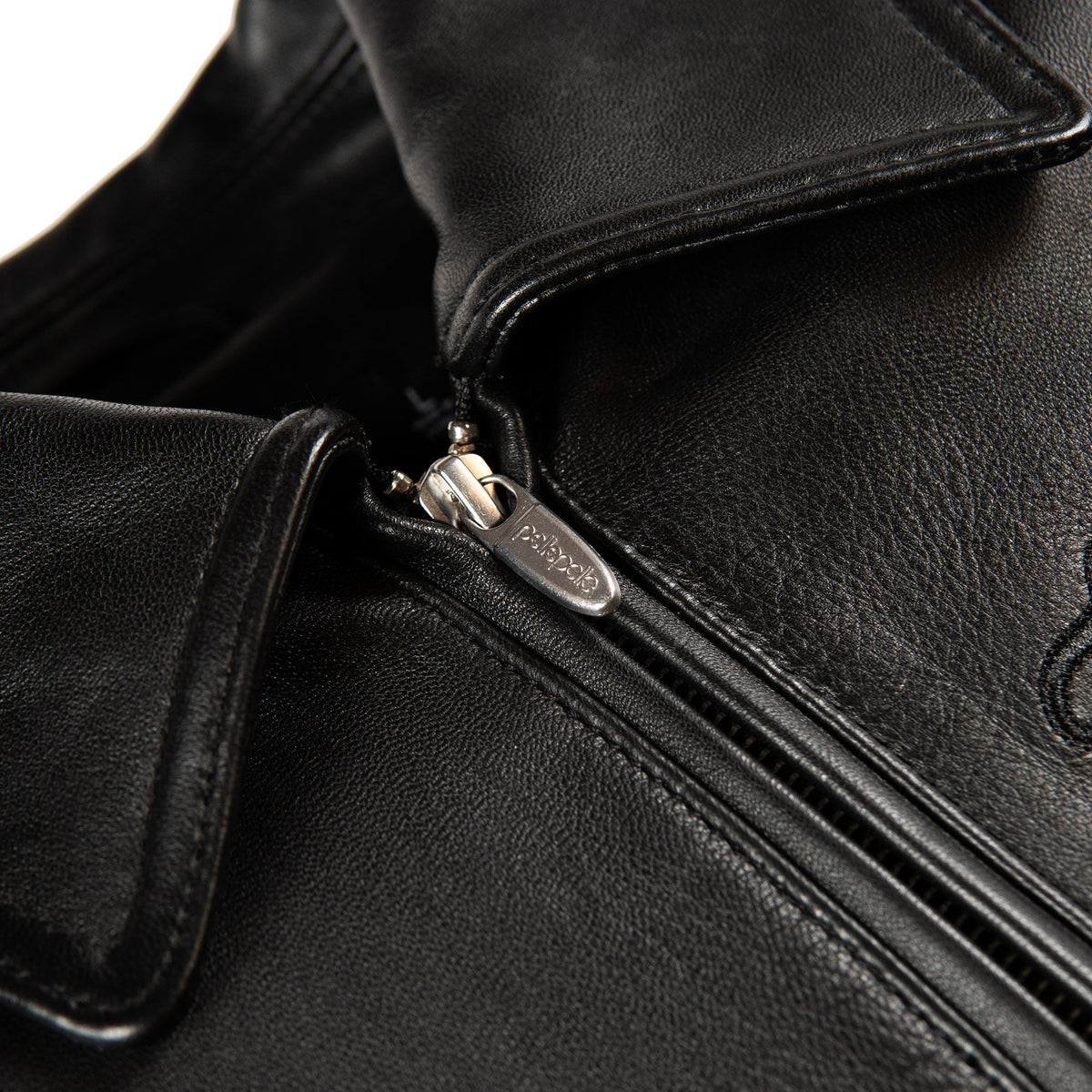 Close-up of a black leather jacket with a silver metal zipper and a visible 'pelle' logo on the zipper pull.