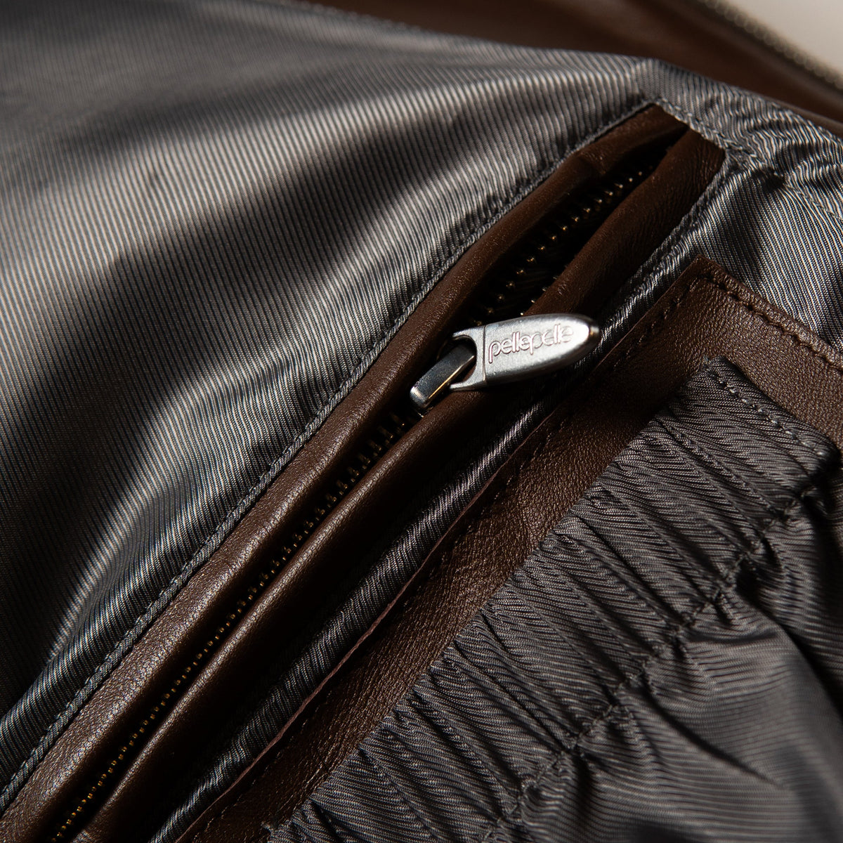 Close-up detail of a brown leather zipper with a silver-tone metal pull engraved with the brand name 'ESTEEL'.