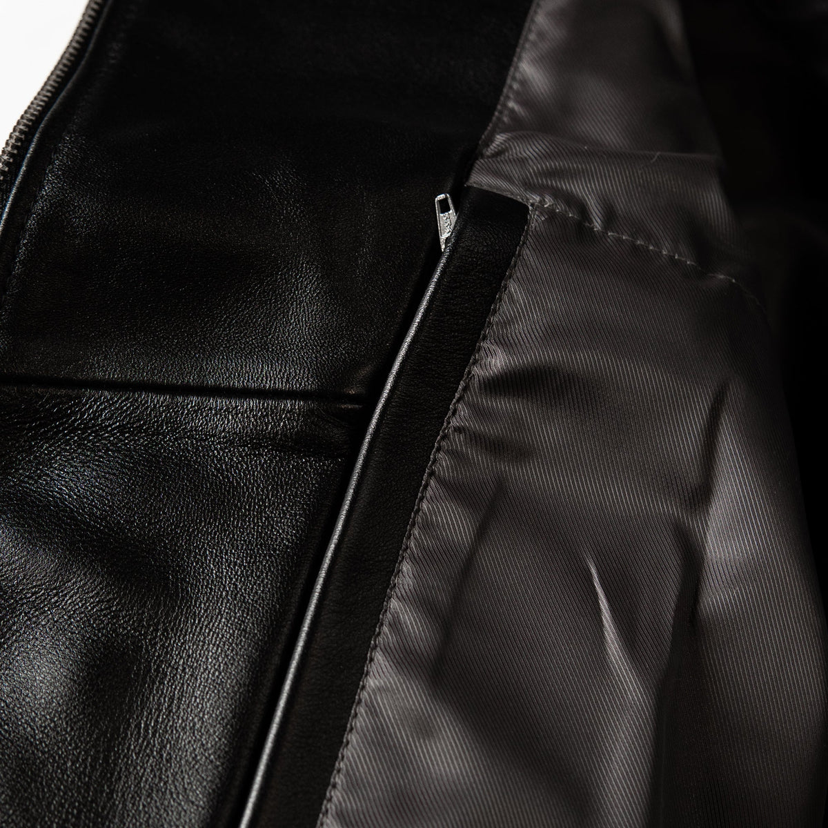 Close-up detail of a black leather jacket showing a black zipper, black fabric lining, and a black metal zipper pull.