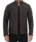 A man wearing a dark brown distressed leather motorcycle jacket with contrast stitching, a stand collar, and zippered chest pockets, paired with a black shirt and black pants against a white background.