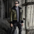 Man wearing a green leather jacket with fur collar, holding a bag, standing in front of an old building.