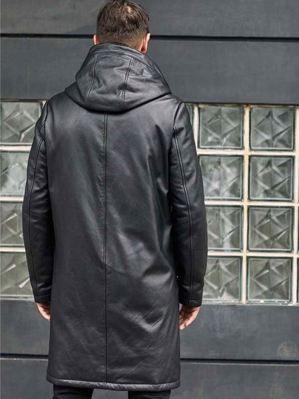 Person wearing a black leather coat standing in front of a glass block wall.