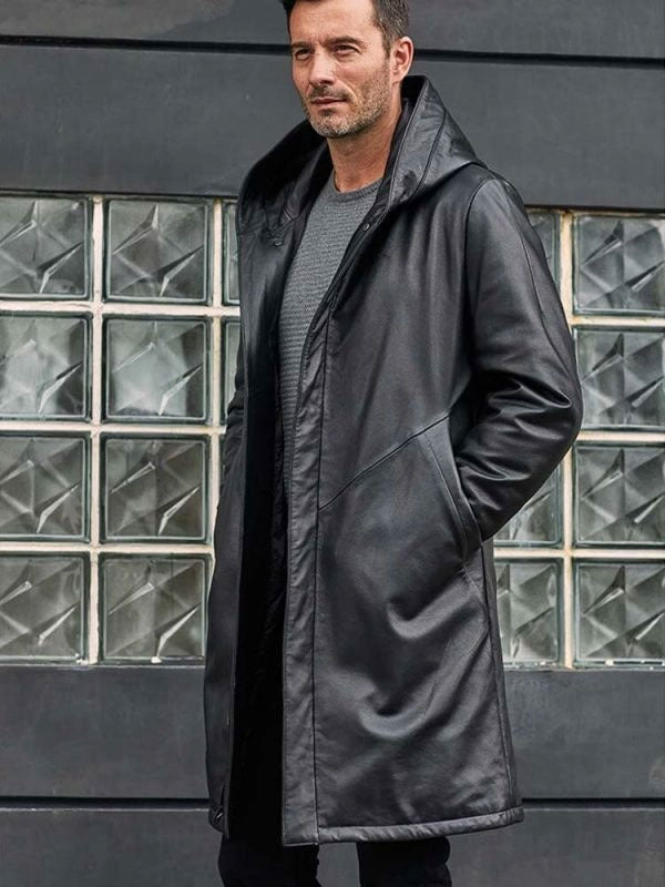 Man wearing a black coat standing in front of a glass-block wall.
