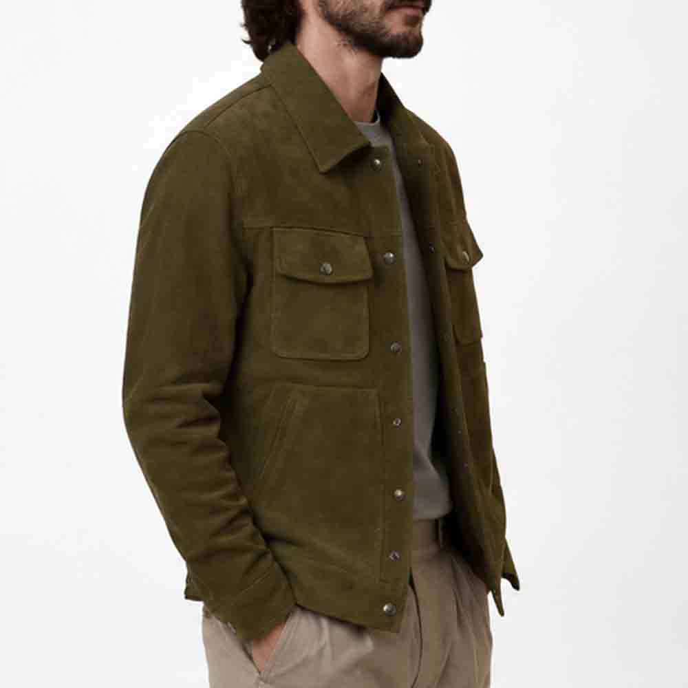 A man wearing an olive green suede jacket over a gray t-shirt and beige trousers, shown from the waist up against a plain white background.