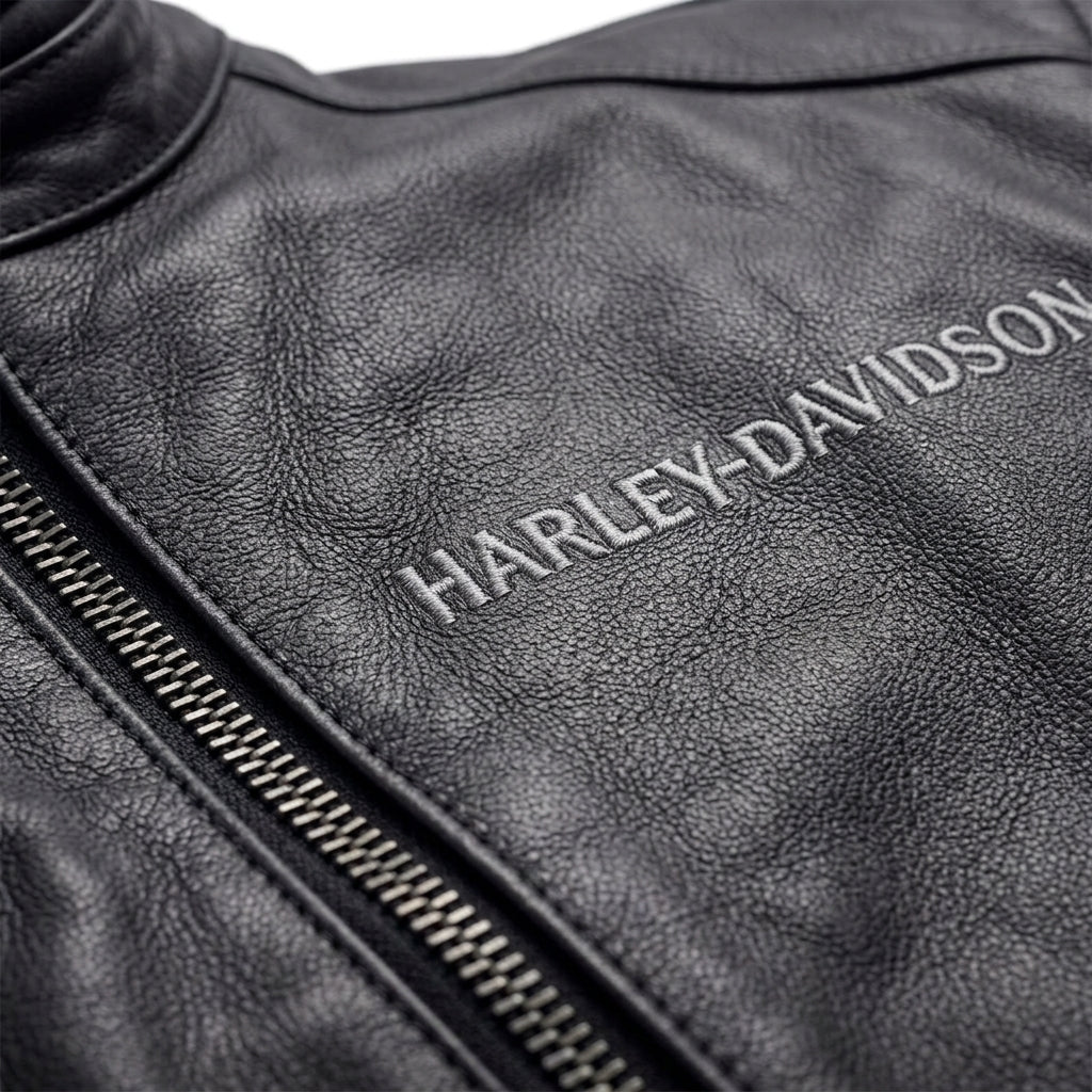 Close-up of a black leather jacket with a silver zipper and a silver embroidered Harley-Davidson logo on the chest.