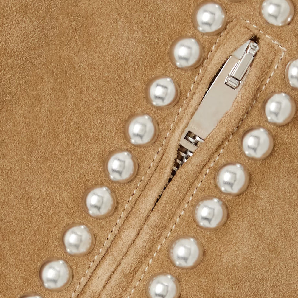 Close-up of a tan suede or suede material with a silver zipper and a row of round pearl-like embellishments running diagonally across the frame.