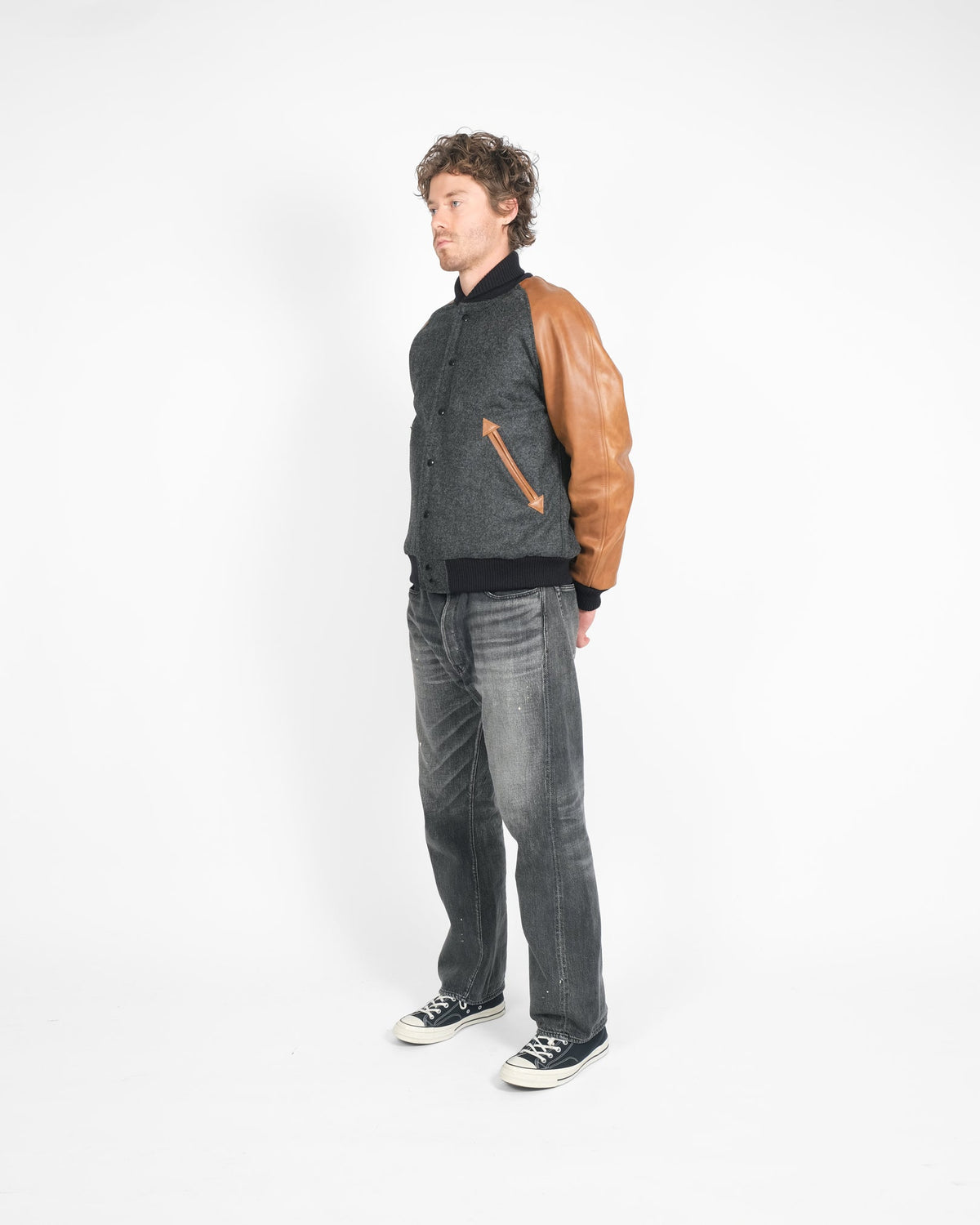 Person wearing a gray jacket with brown leather sleeves and gray jeans on a white background
