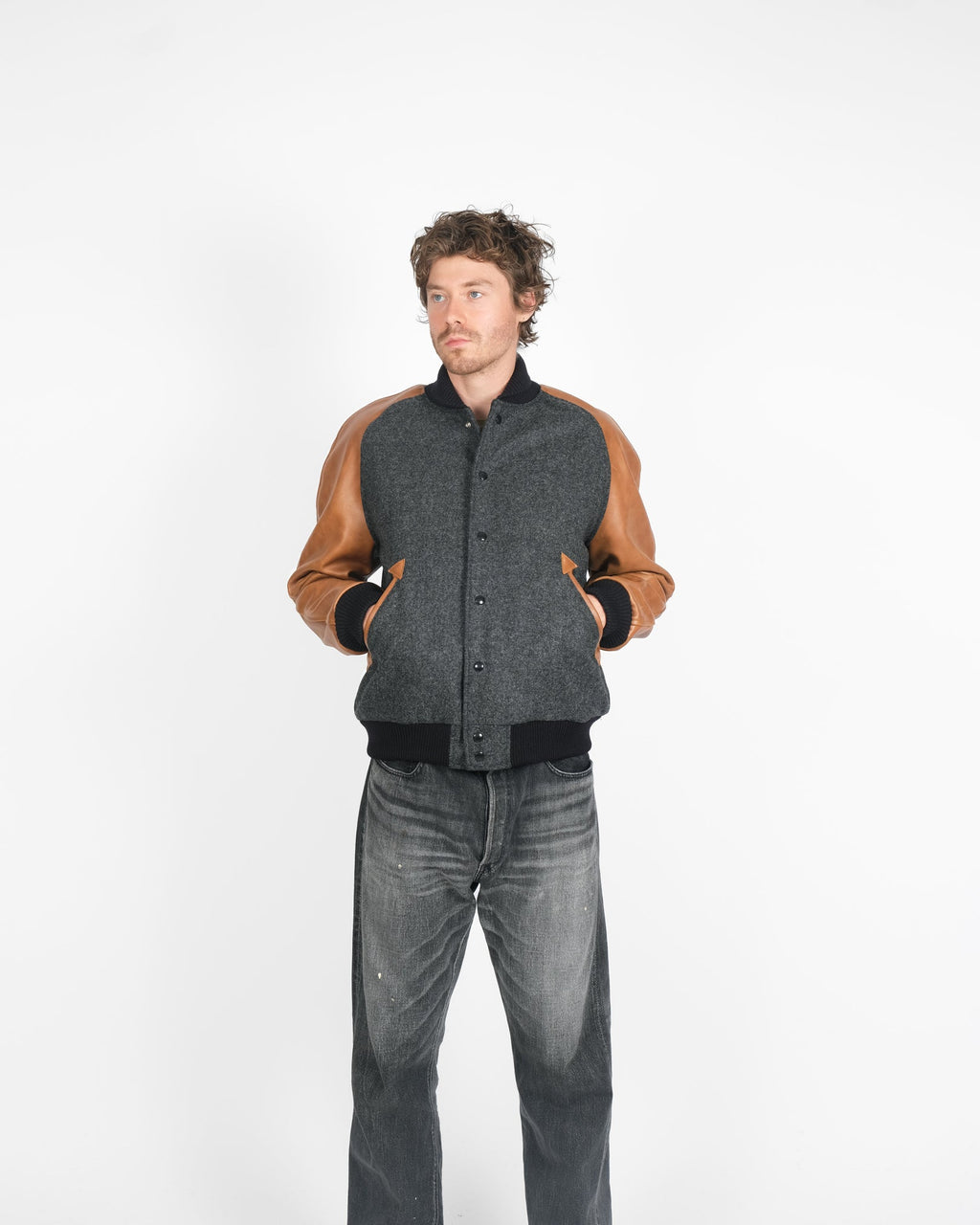 Man wearing a gray and brown varsity jacket on a white background