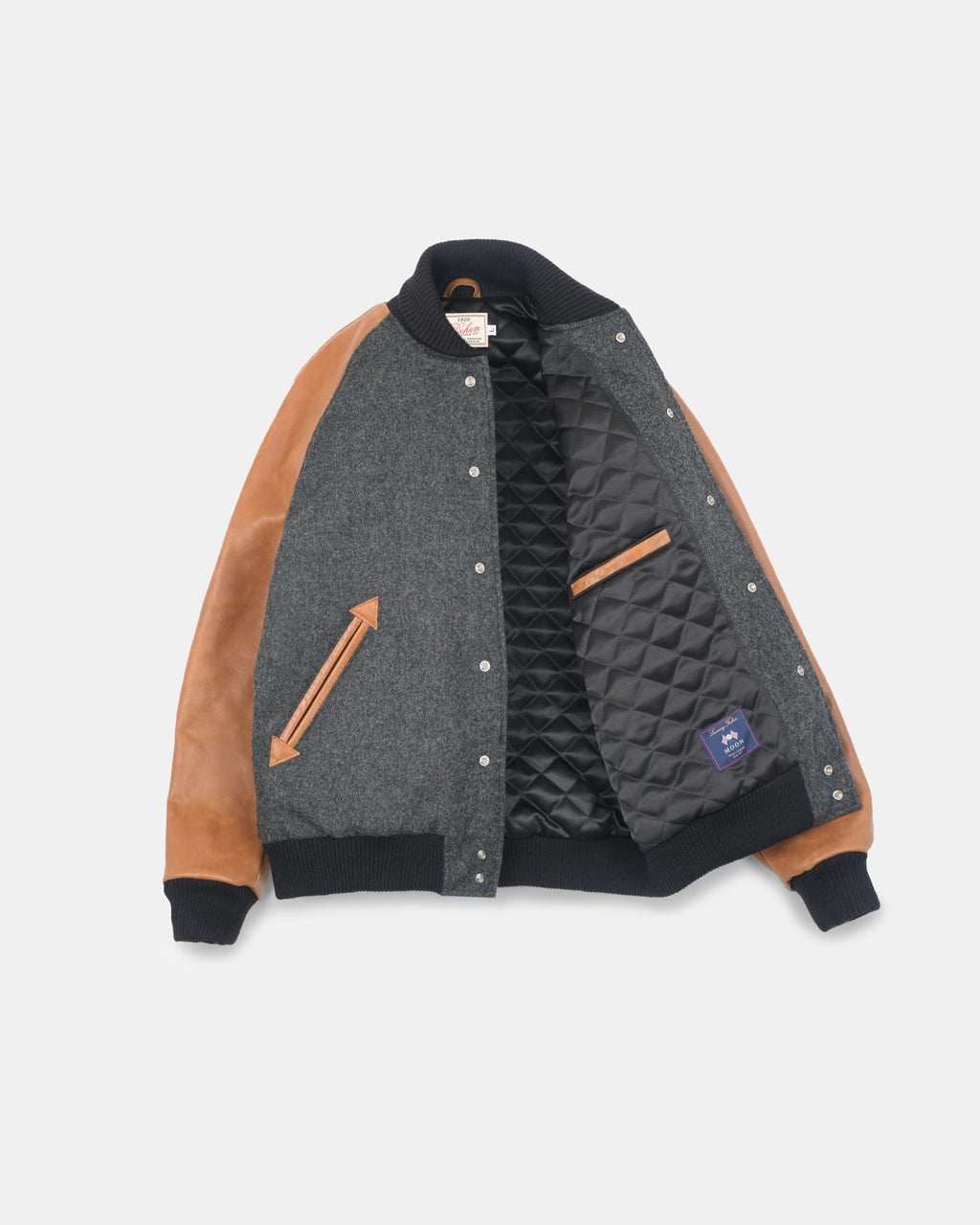 A color-blocked bomber jacket featuring a dark gray wool body, tan leather sleeves, and a black quilted lining, displayed flat against a light gray background.