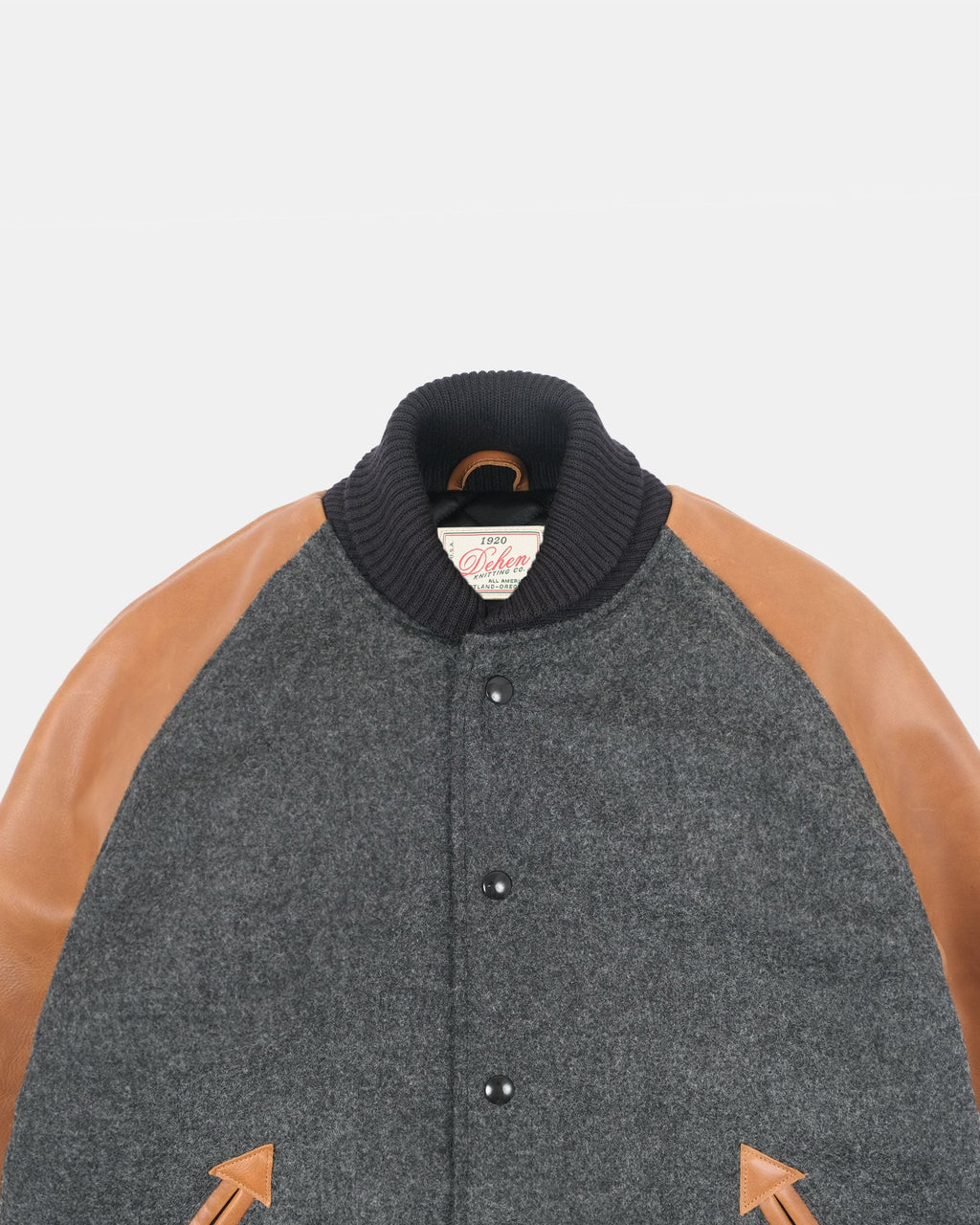 A close-up of a wool-blend varsity jacket with a dark gray body, tan leather sleeves, and a black ribbed knit collar. The brand label on the collar reads 'Cotton & Wool'.