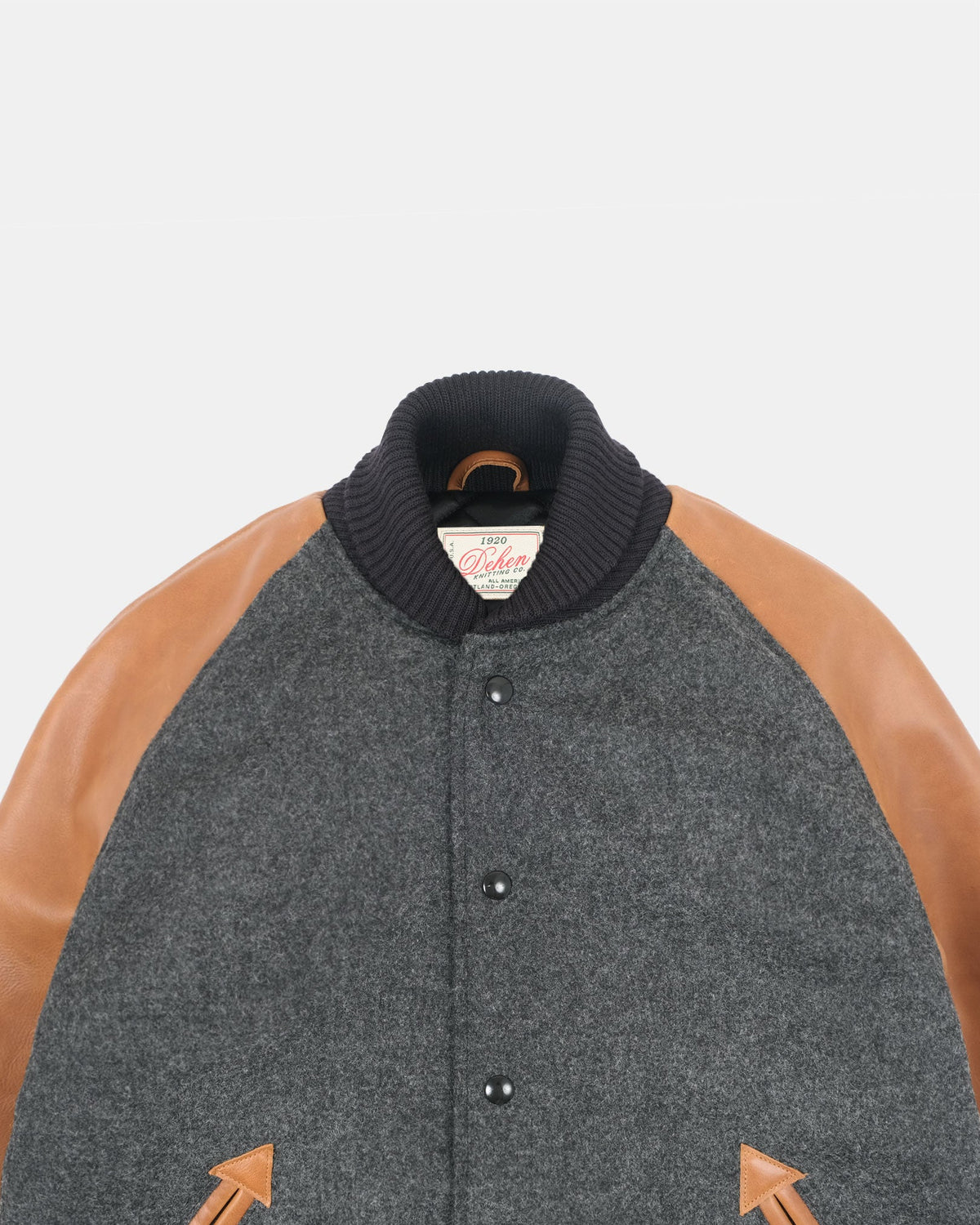 A close-up of a wool-blend varsity jacket with a dark gray body, tan leather sleeves, and a black ribbed knit collar. The brand label on the collar reads 'Cotton & Wool'.