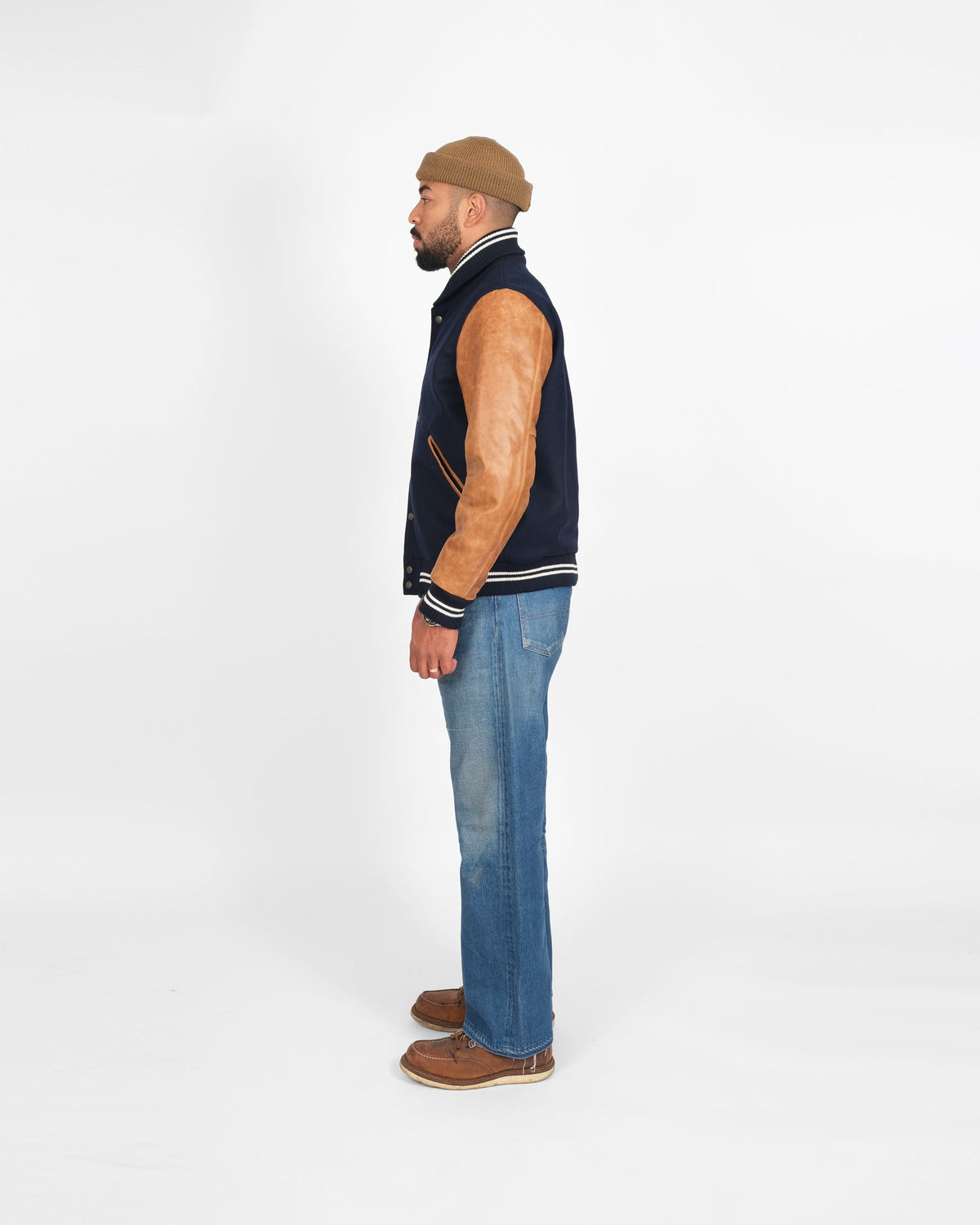 Man wearing a navy blue vest, sleeveless shirt, and jeans on a white background