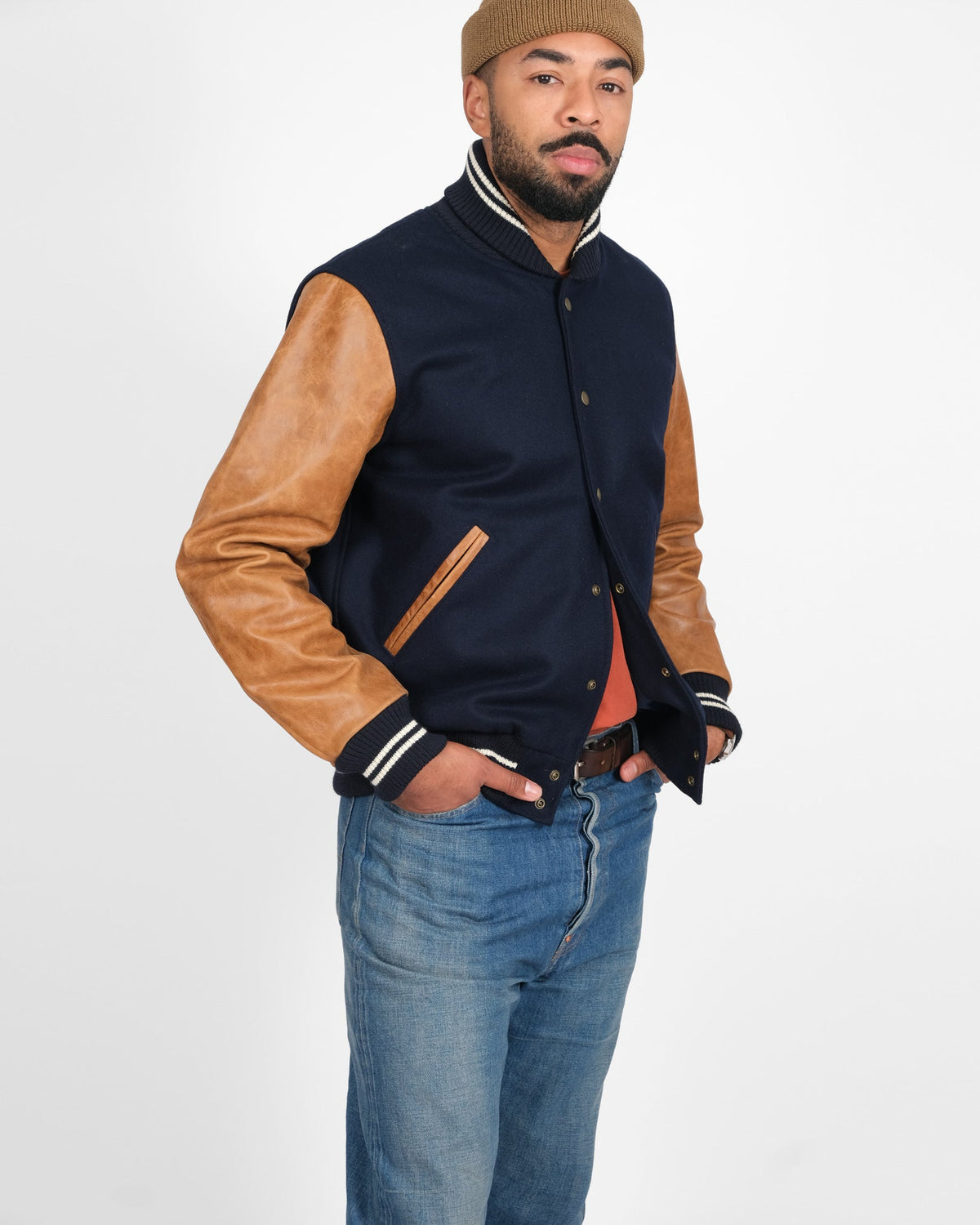 Man wearing a navy jacket with brown sleeves and jeans on a white background