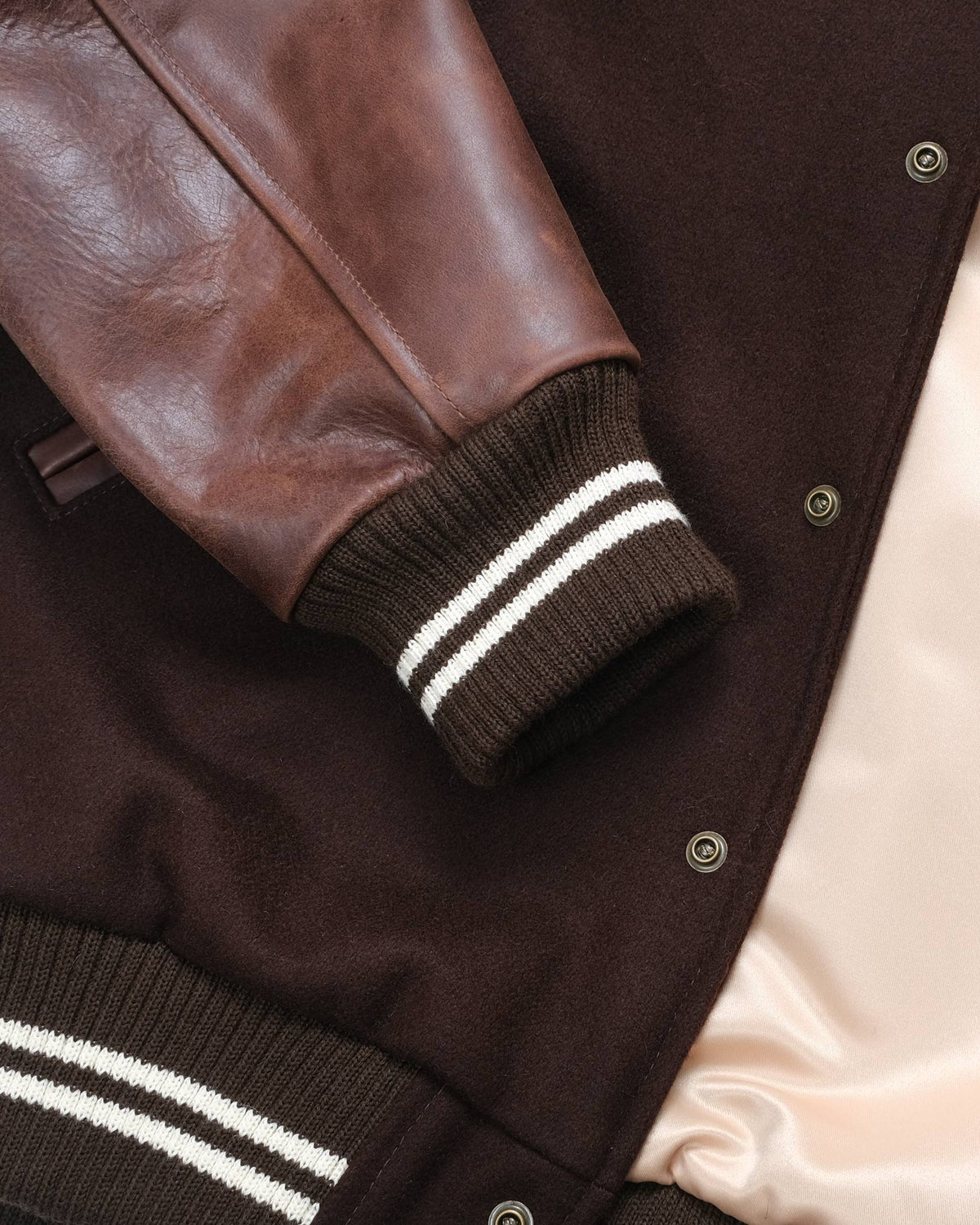 Close-up of a brown leather jacket with white stripes on the cuffs and collar.